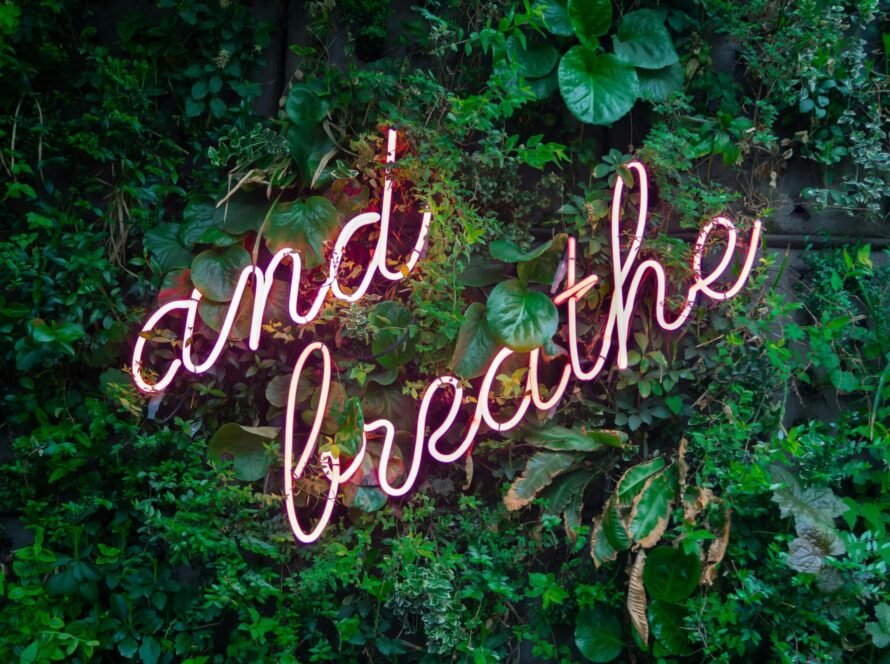 a neon sign on a wall of plants
